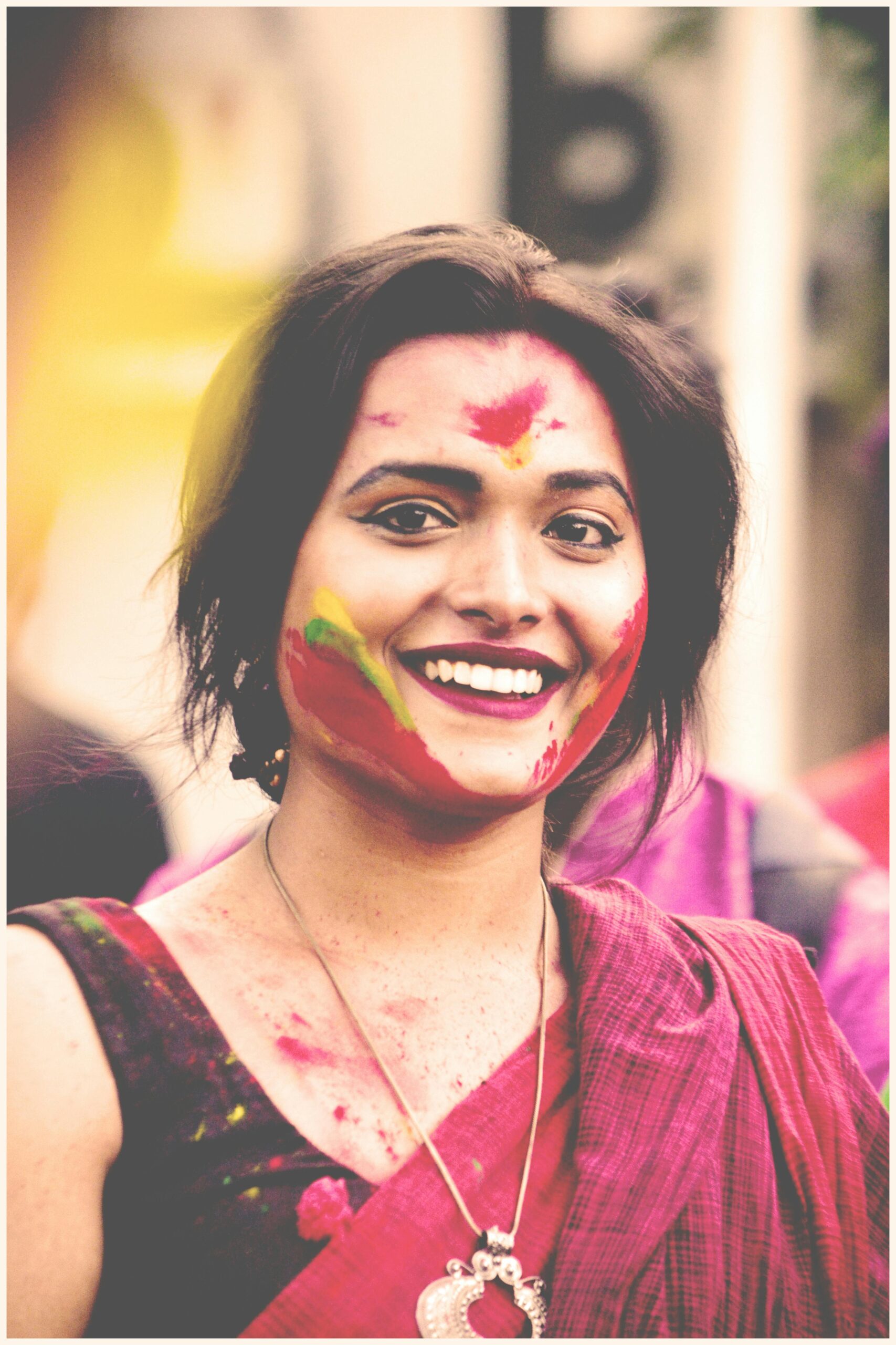 Vibrant portrait of a smiling woman with colorful face paint at Holi festival.