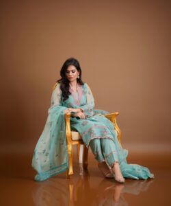 A woman in a beautifully embroidered dress sitting elegantly indoors on a golden chair.