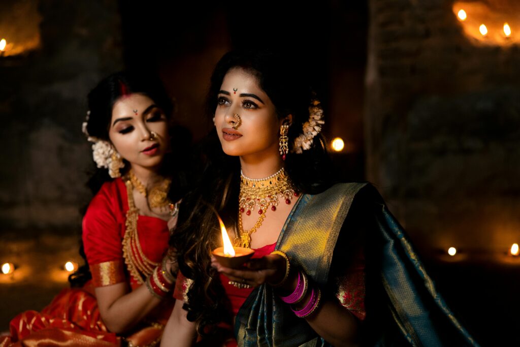 Two Indian women in sarees holding a diya, capturing the essence of elegance and tradition.